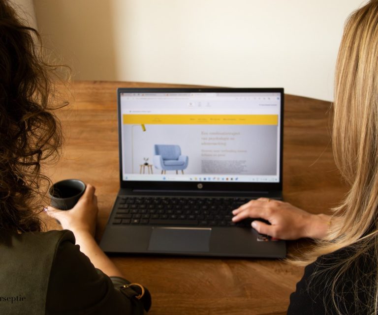 Geen wachtlijst - ACT en Adem Twee mensen bekijken de ACT en Adem website op een laptop terwijl ze aan een houten tafel zitten.